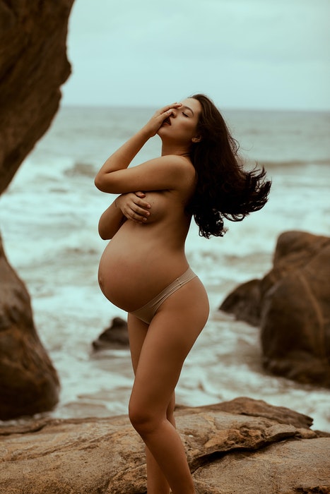Hermosa foto de tocador de maternidad de una mujer embarazada posando desnuda en la playa