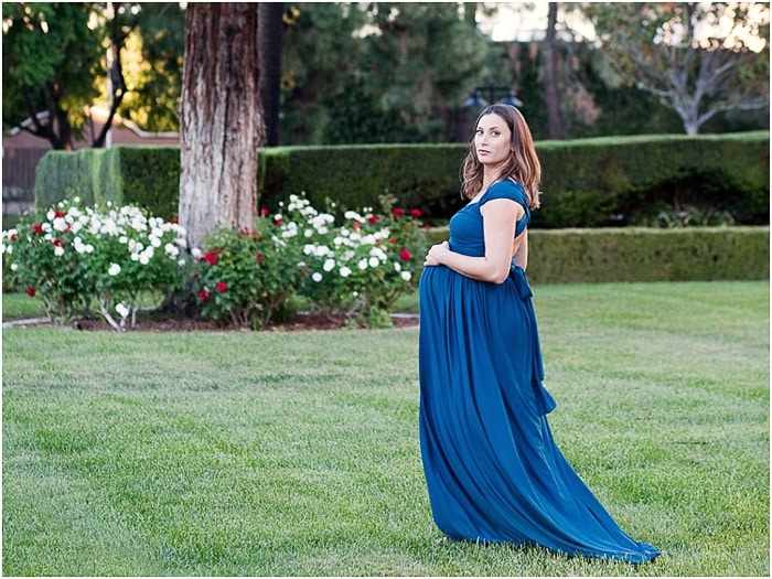 Una mujer en vestido de noche azul al aire libre posando para una sesión de fotografía de maternidad