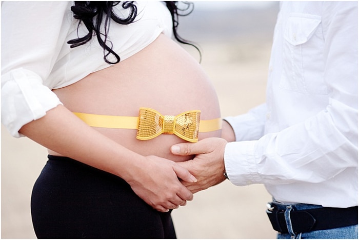 Un primer plano de un hombre acunando el vientre de la esposa embarazada en sus manos, una cinta amarilla y dorada brillante en su vientre
