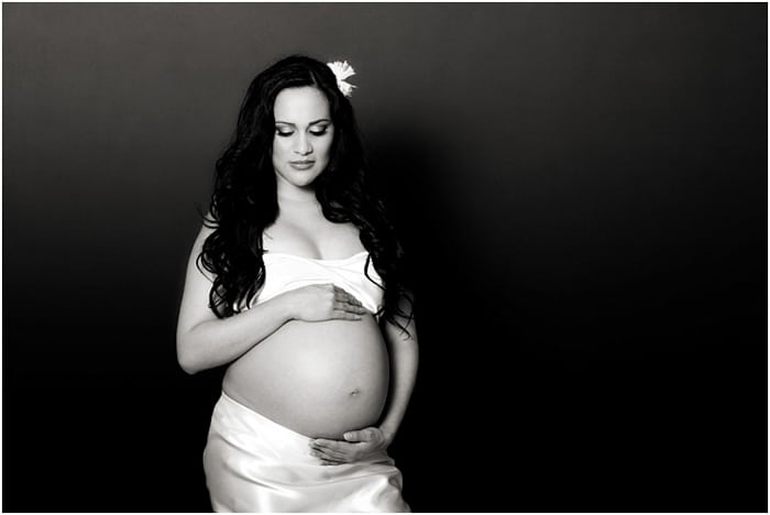 Mujer embarazada vestida de blanco, una flor en el pelo, acunando su vientre