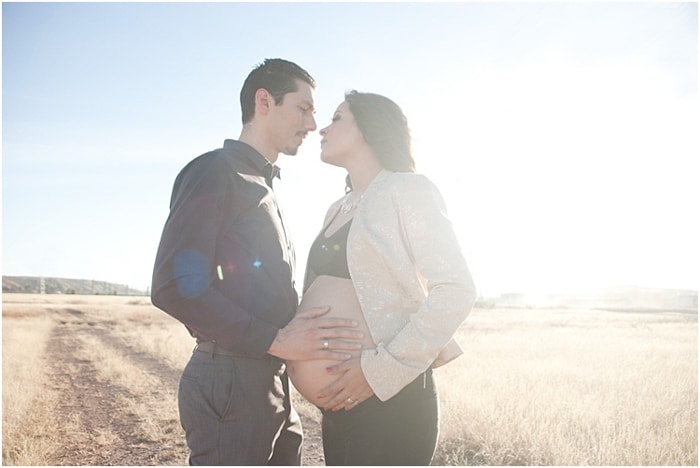 Una foto romántica de una pareja embarazada al aire libre, el sol brillante detrás de ellos