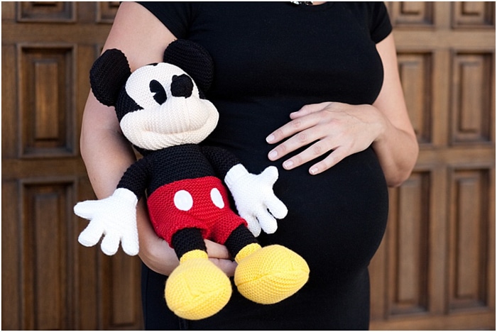 Cerrar mujer embarazada sosteniendo su vientre, sosteniendo un juguete de peluche de Mickey Mouse junto a ella