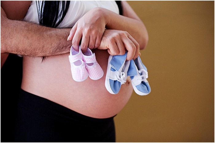 Cerrar pareja abrazando el vientre de embarazada, sosteniendo zapatos de bebé de color rosa y azul