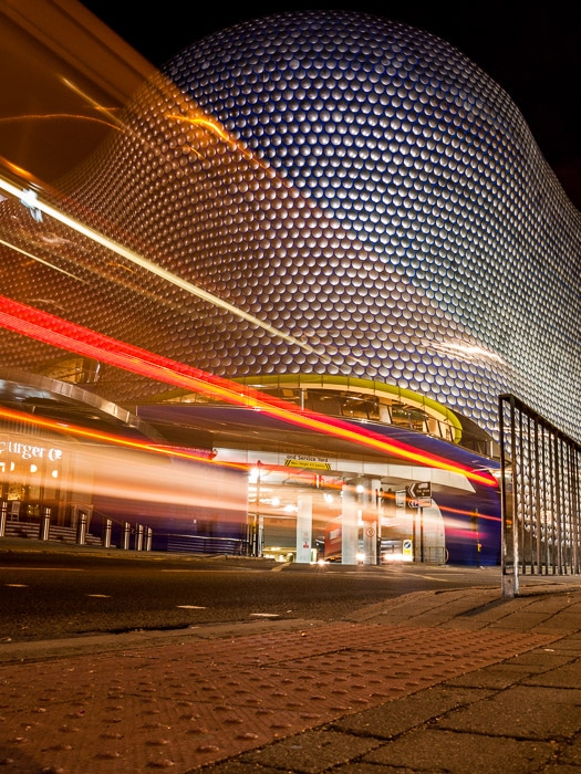 El desenfoque de movimiento de color de estelas de luz en frente del centro comercial Bullring en Birmingham, Reino Unido.