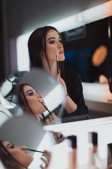 Un retrato díptico de una modelo femenina morena reflejada en varios espejos mientras se aplica el maquillaje