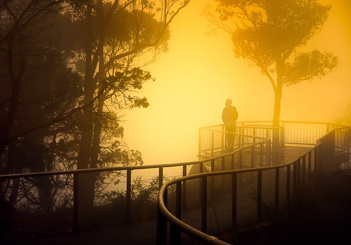 Una persona en un puente en un paisaje neblinoso al atardecer