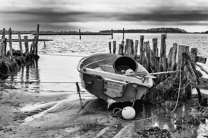 Fotografía costera en blanco y negro que muestra un bote pequeño con marea baja.