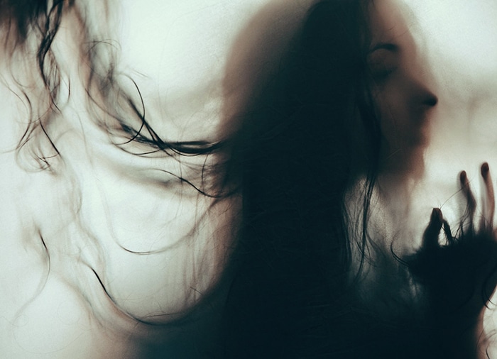 Retrato borroso atmosférico de una modelo femenina de mal humor con el pelo que cubre su rostro - ejemplos de retratos oscuros