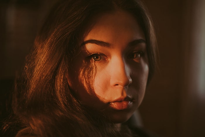 Retrato atmosférico de una modelo femenina de mal humor mirando directamente a la cámara con poca luz - ejemplos de retratos oscuros