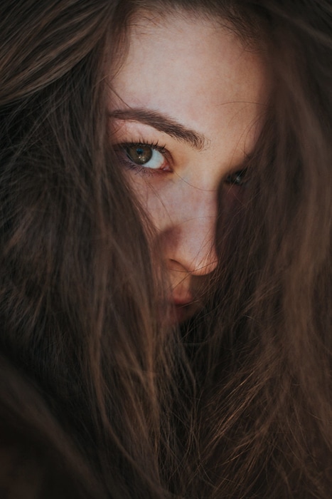 Retrato de primer plano atmosférico de un modelo femenino de mal humor con el pelo que cubre su rostro - ejemplos de retratos oscuros