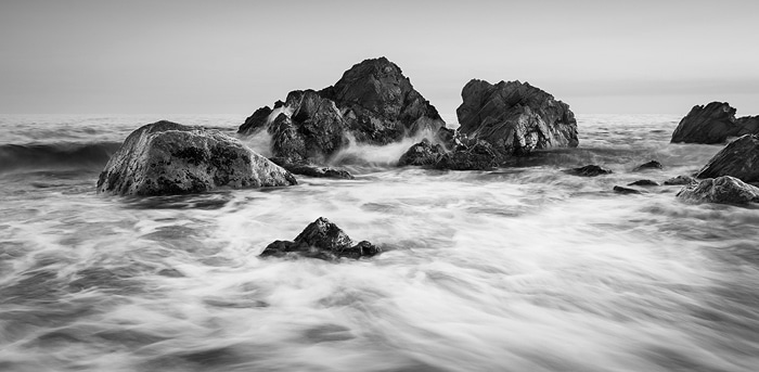 Imagen en blanco y negro de rocas a la orilla del mar que muestra un hermoso contraste