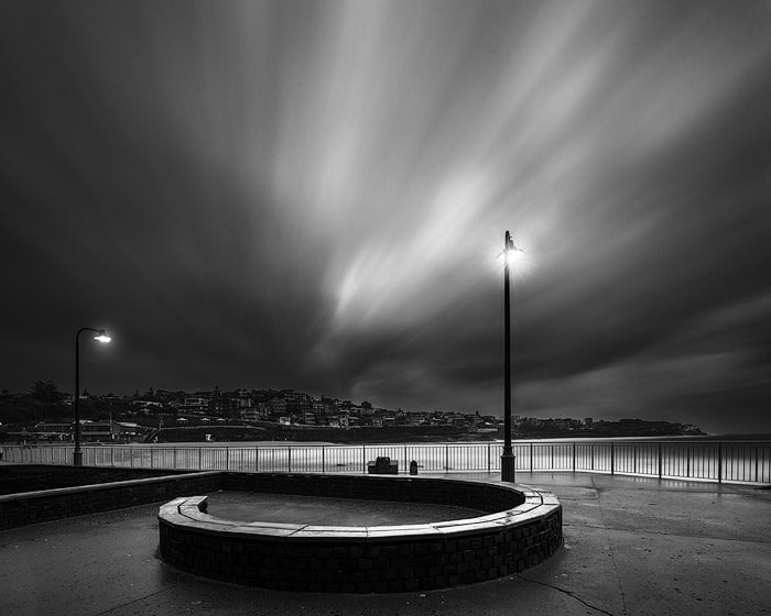 Fotografía de larga exposición en blanco y negro de una playa iluminada por lámparas en la noche