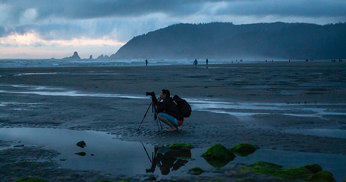 Un fotógrafo configurando un trípode en una playa con poca luz