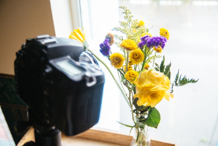 una cámara réflex digital configurada para tomar una foto macro de un ramo de flores en el alféizar de una ventana: consejos de iluminación para fotografía macro