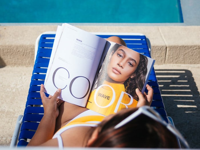 Una niña leyendo una revista de moda mientras toma el sol en una tumbona