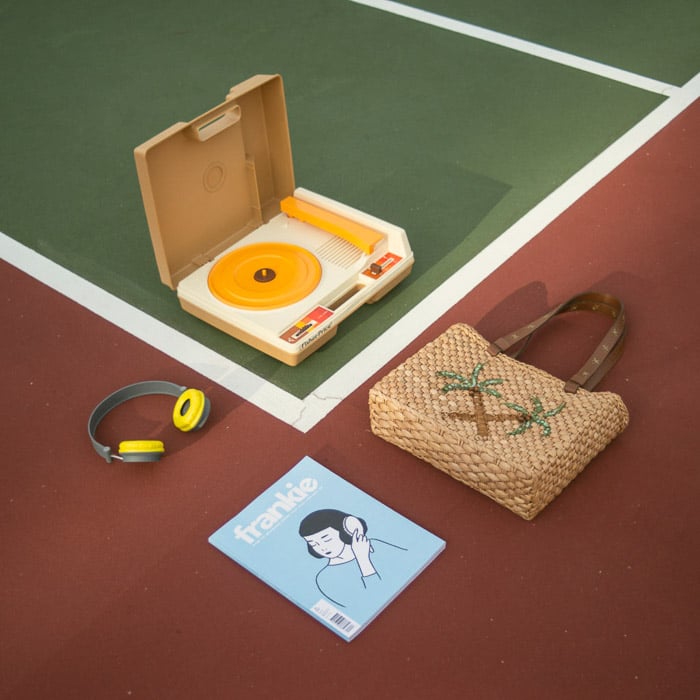 Fotografía cenital de un tocadiscos, bolso, revista y auriculares dispuestos en una pista deportiva
