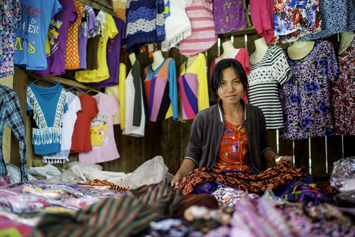 Una vendedora del mercado en su puesto, con un ajetreado fondo desordenado de ropa y material de colores
