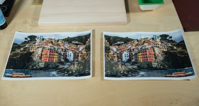 Dos fotos idénticas de una ciudad costera de colores brillantes, descansando sobre una tabla de madera preparándose para transferir la foto a la madera