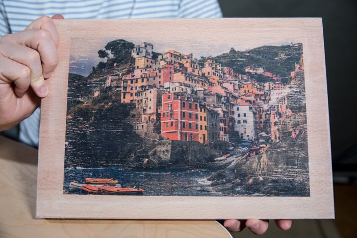 Un hombre que sostiene una tabla de madera con una colorida foto de la ciudad costera transferida a ella