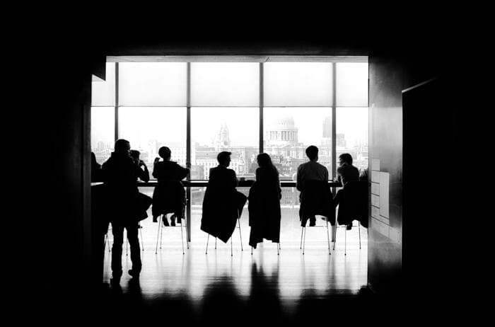 Una foto atmosférica en blanco y negro que mira hacia un aula o una oficina llena de gente en los escritorios.