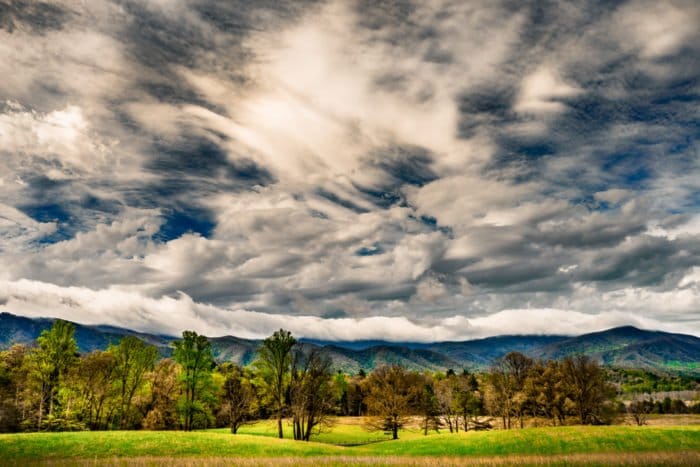 Clima dramático: cielo amplio con múltiples tipos de nubes sobre colinas, campos y bosques