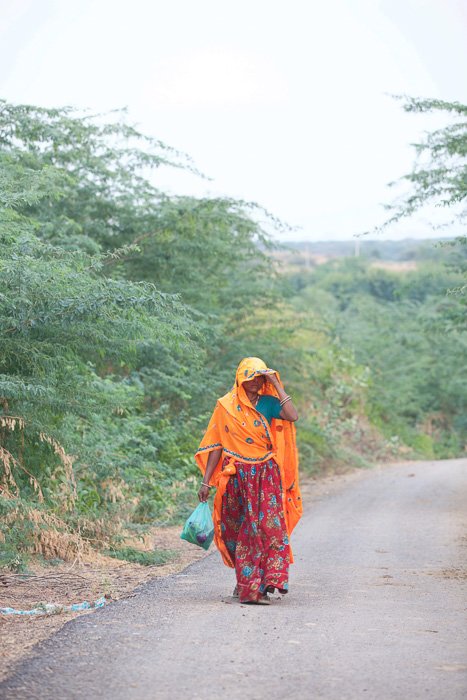 Fotografía de viaje de una mujer vestida de naranja y rojo caminando por la India.