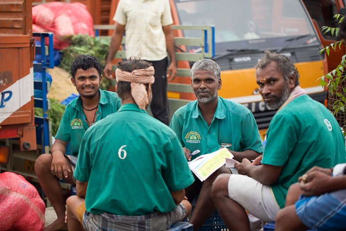 Fotografía de viaje de 4 hombres vestidos de verde sentados en un mercado de flores en la India.