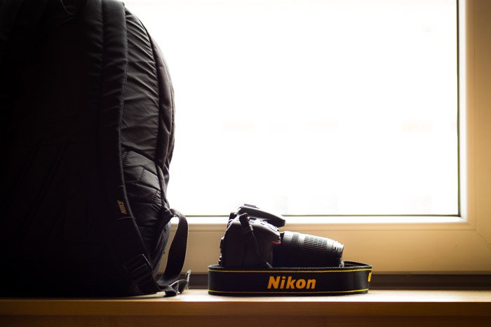 Una cámara Nikon colocada en un estante al lado de una mochila para cámara. 