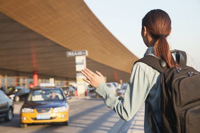 mujer morena con una mochila llamando a un taxi en el aeropuerto