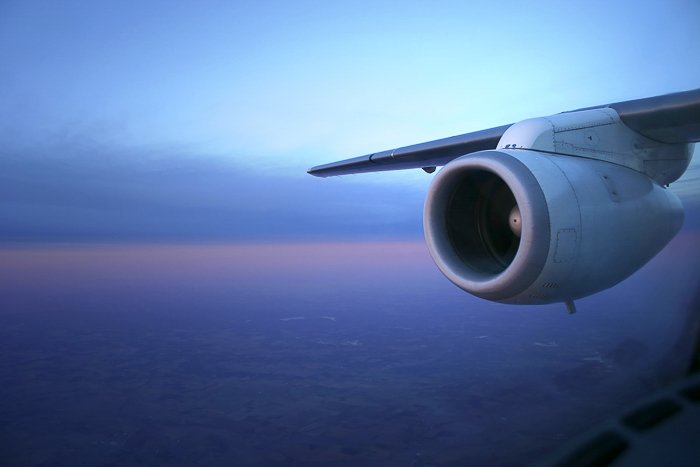 Vista desde la ventana de un avión del ala y el motor del avión, contra un atardecer azul, morado y naranja