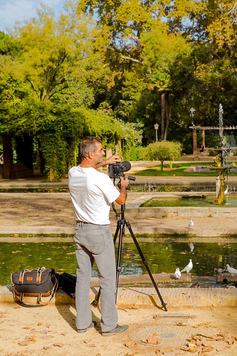 foto de atrás de un hombre instalando una DSLR en un trípode junto a un estanque con pájaros blancos, los árboles en la distancia - consejos de seguridad para viajes