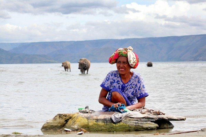 Fotografía de viaje de una mujer lavando ropa en el mar con vacas en el fondo: lista de verificación de fotografía de viaje.
