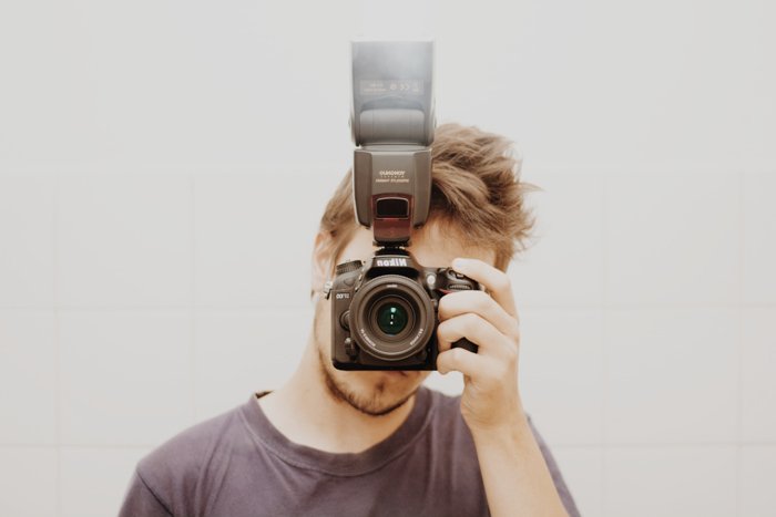 Foto de un chico sosteniendo una cámara con flash externo frente a su cara