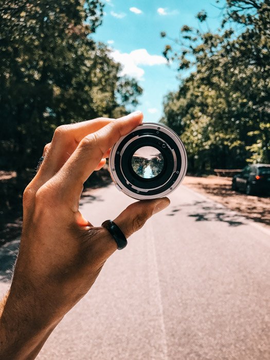 Una mano sosteniendo la lente de la cámara que muestra una calle de la ciudad con árboles al costado