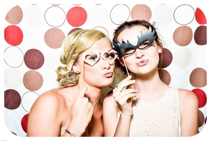 dos jóvenes posando con máscaras frente a un colorido fondo fotográfico