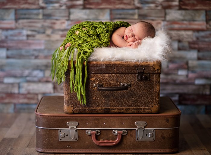 Pequeño bebé recién nacido durmiendo en maletas rústicas
