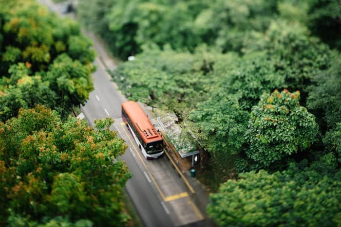 Una foto de cambio de inclinación de un autobús estacionado en una carretera en una hermosa zona rural rodeada de árboles