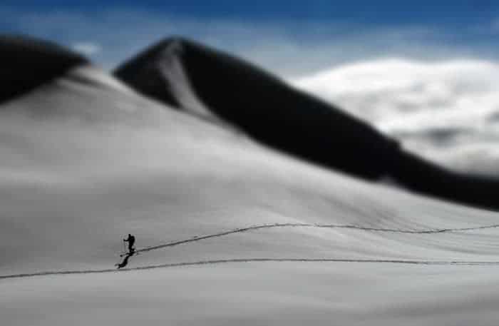 Una persona esquiando cuesta abajo con una montaña nevada detrás, tomada con una lente de fotografía con cambio de inclinación.