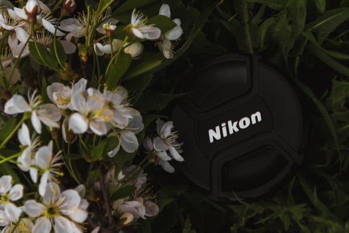 Primer plano de una tapa de lente Nikon entre flores