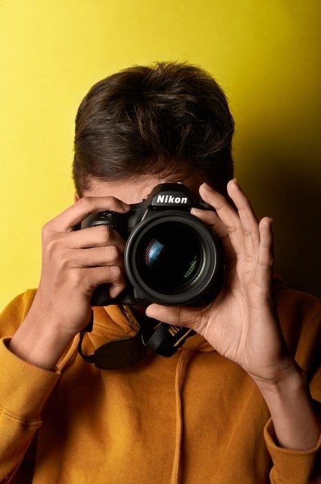 hombre disparando con una Nikon DSLR con un fondo amarillo