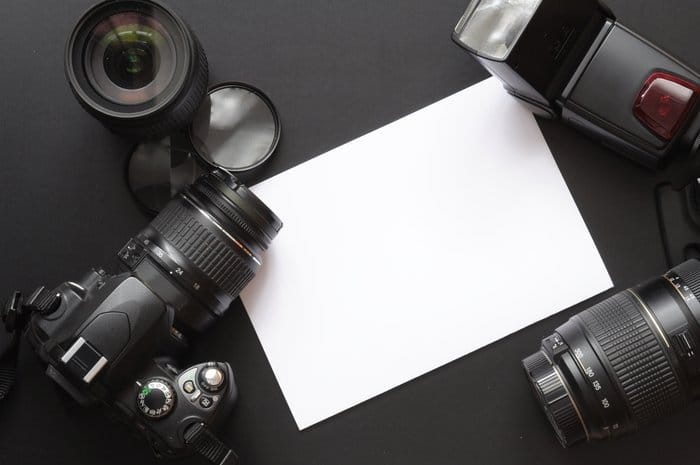 Foto de una cámara, lentes y una hoja de papel en blanco.