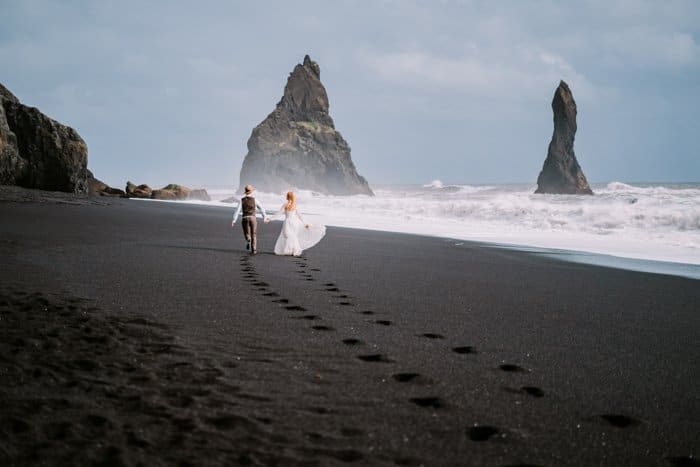 Una imagen de una pareja casada caminando de la mano en una playa de arena negra