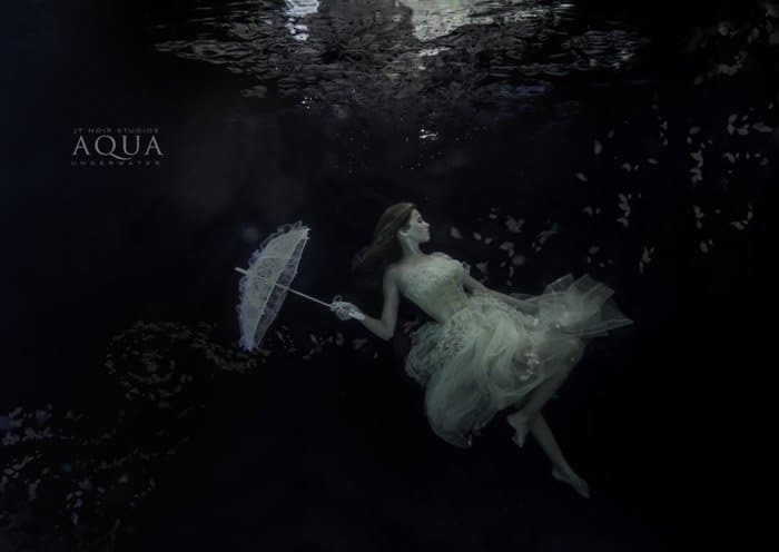 Sesión de fotos submarina atmosférica de una modelo femenina sosteniendo un paraguas bajo el agua