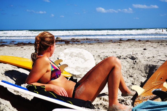 Mujer en bikini descansando en la playa mirando el mar azul
