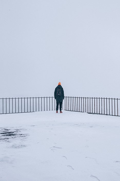 Un retrato de invierno cubierto de nieve de una figura de pie junto a una valla