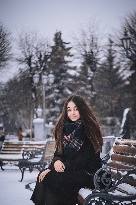 Retrato de invierno atmosférico de un modelo femenino posando en un banco en la nieve que cae