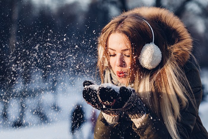 Cerrar fotografía de retrato de invierno de un modelo femenino posando juguetonamente en la nieve que cae