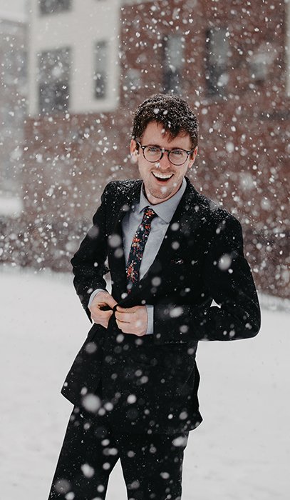 Retrato de invierno divertido de un modelo masculino posando casualmente bajo la nieve que cae