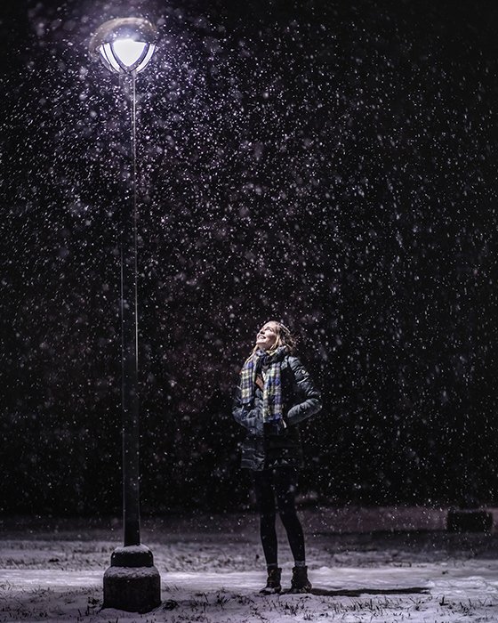 Atmospher retrato de invierno de un modelo femenino posando bajo la nieve que cae en la noche