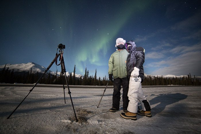 Foto de dos fotógrafos con cámara y trípode fotografiando la aurora boreal.  Fotografía de invierno.